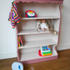 Vintage oudroze boekenkastje voor kinderkamer met sierlijke afwerking en open planken.