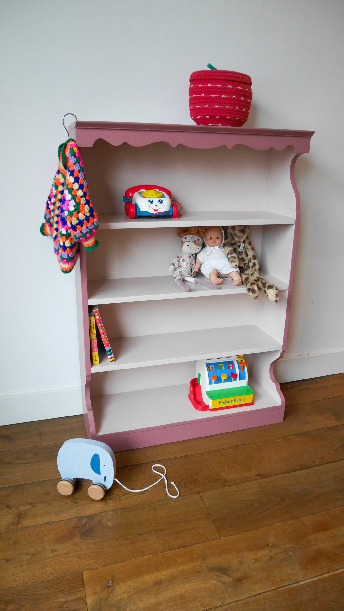 Vintage oudroze boekenkastje voor kinderkamer met sierlijke afwerking en open planken.