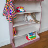 Vintage oudroze boekenkastje voor kinderkamer met sierlijke afwerking en open planken.