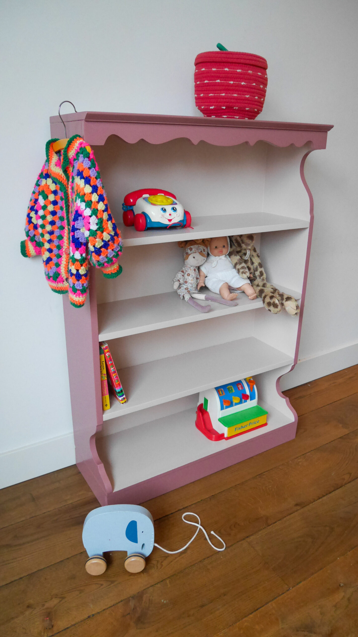 Vintage oudroze boekenkastje voor kinderkamer met sierlijke afwerking en open planken.