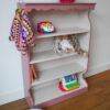Vintage oudroze boekenkastje voor kinderkamer met sierlijke afwerking en open planken.