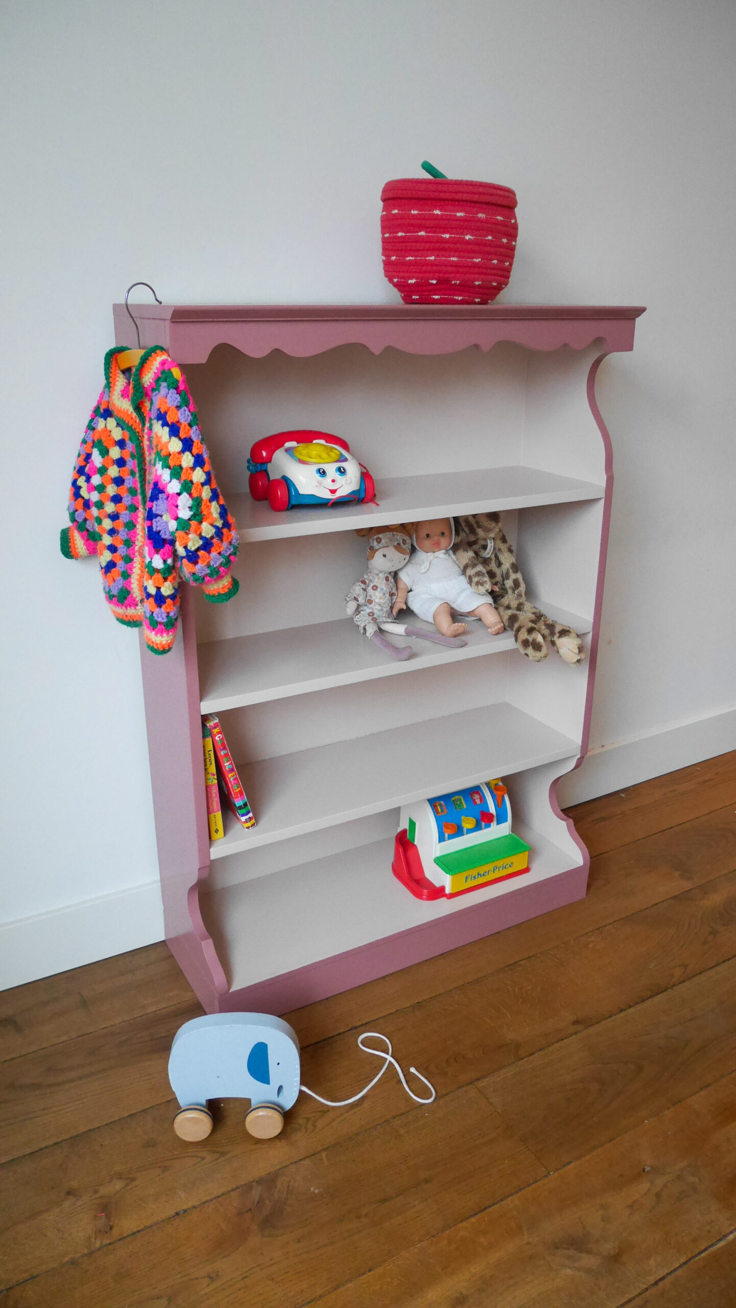 Vintage oudroze boekenkastje voor kinderkamer met sierlijke afwerking en open planken.