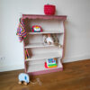 Vintage oudroze boekenkastje voor kinderkamer met sierlijke afwerking en open planken.