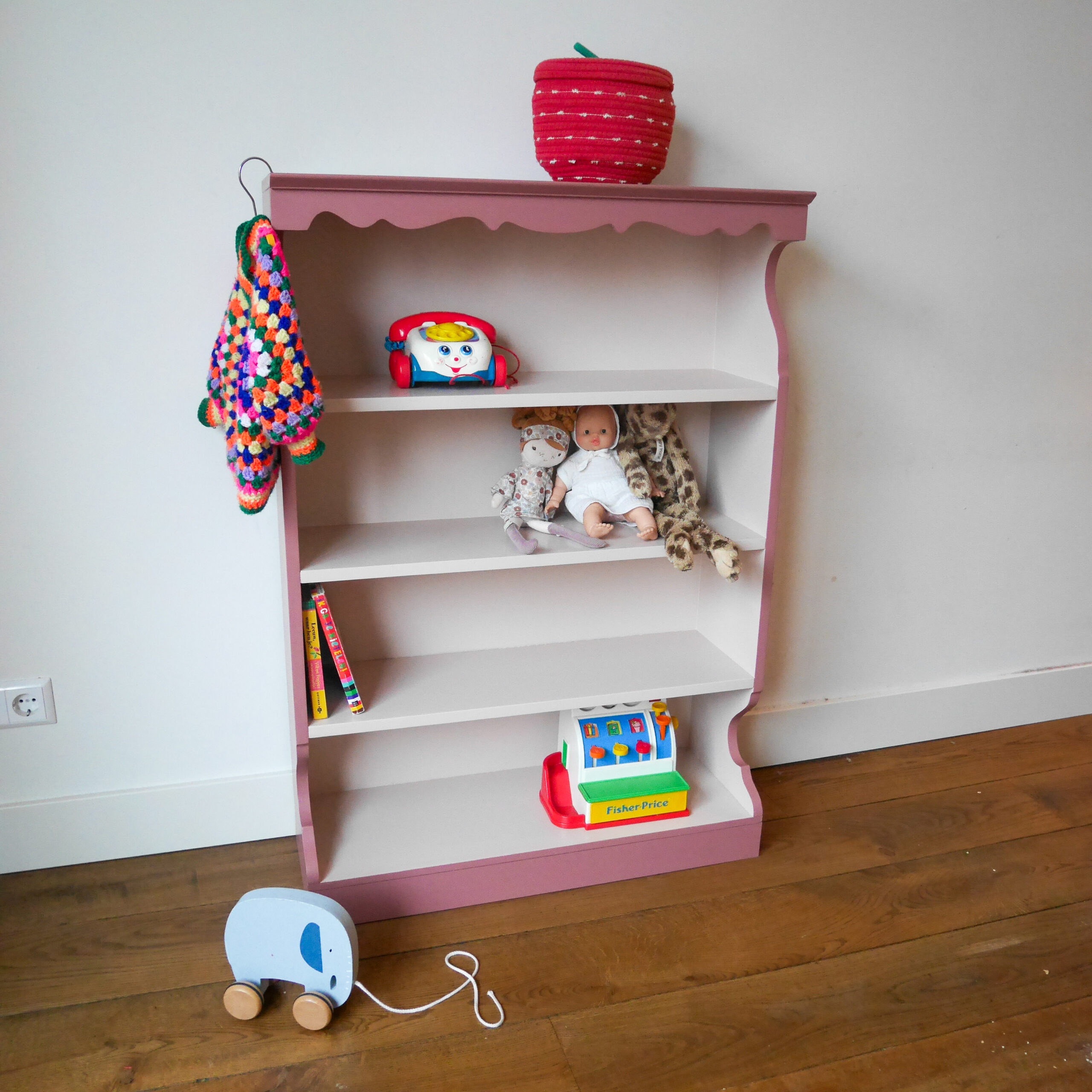 Vintage oudroze boekenkastje voor kinderkamer met sierlijke afwerking en open planken.