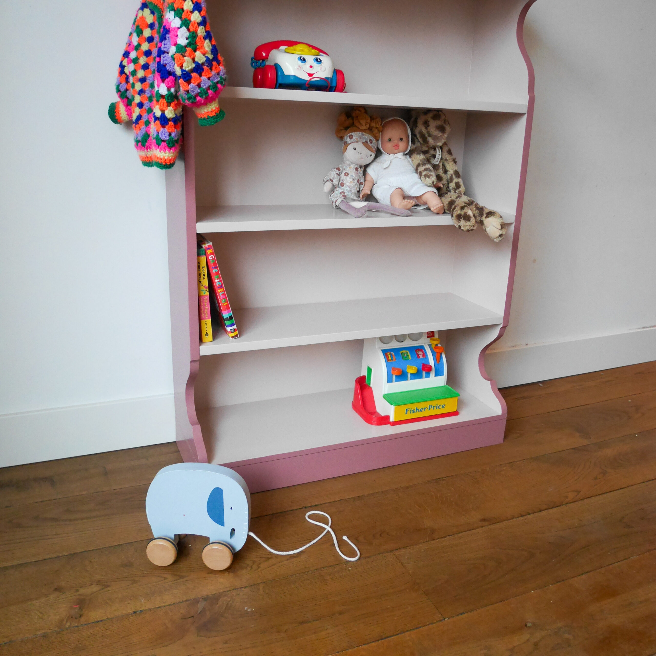 Vintage oudroze boekenkastje voor kinderkamer met sierlijke afwerking en open planken.