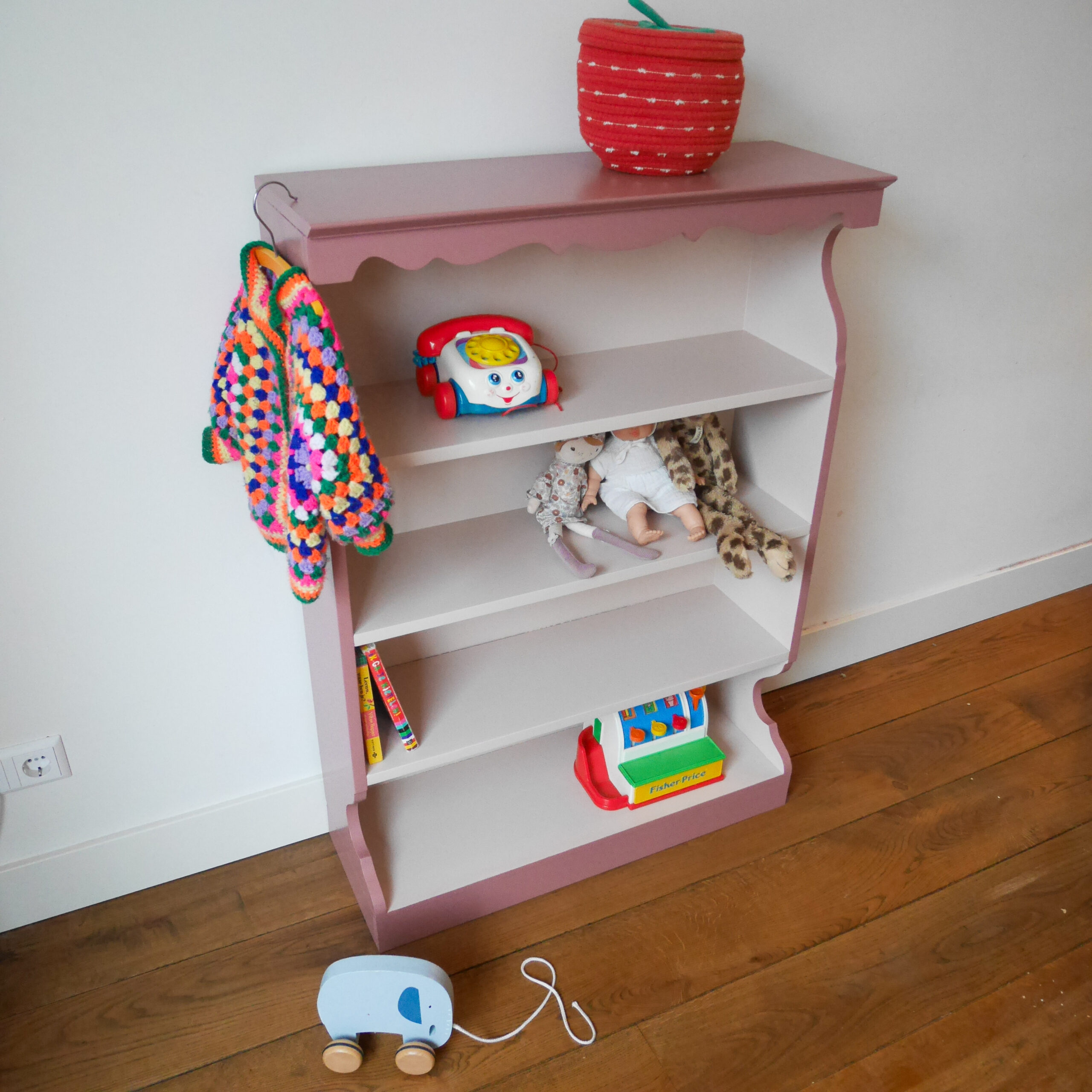 Vintage oudroze boekenkastje voor kinderkamer met sierlijke afwerking en open planken.