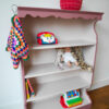 Vintage oudroze boekenkastje voor kinderkamer met sierlijke afwerking en open planken.