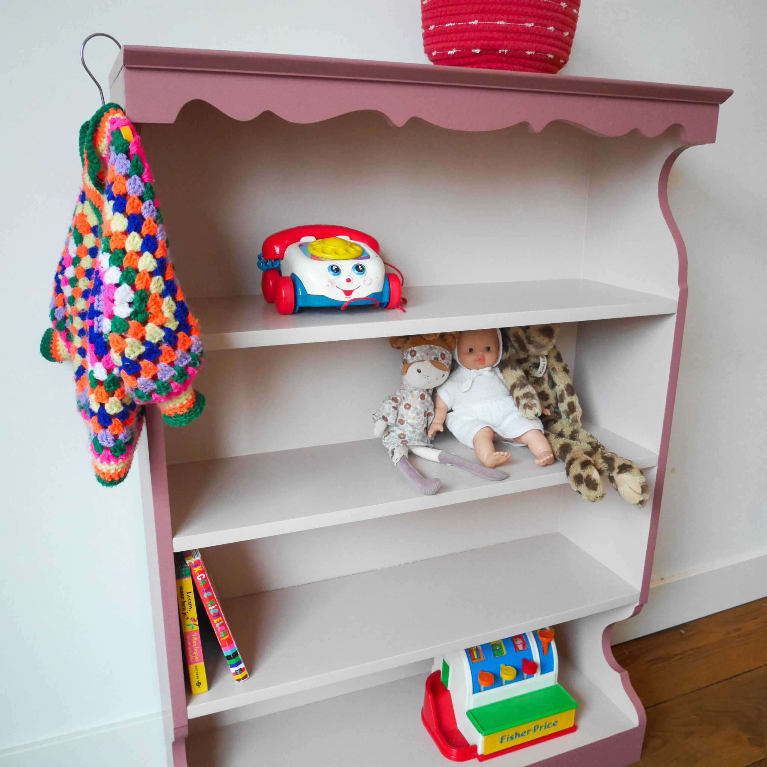 Vintage oudroze boekenkastje voor kinderkamer met sierlijke afwerking en open planken.