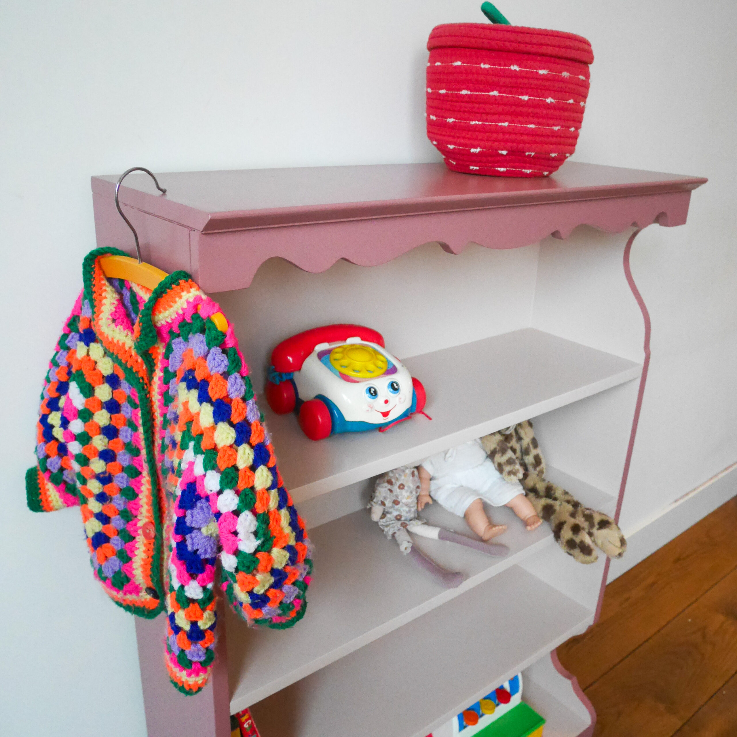 Vintage oudroze boekenkastje voor kinderkamer met sierlijke afwerking en open planken.