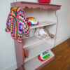 Vintage oudroze boekenkastje voor kinderkamer met sierlijke afwerking en open planken.