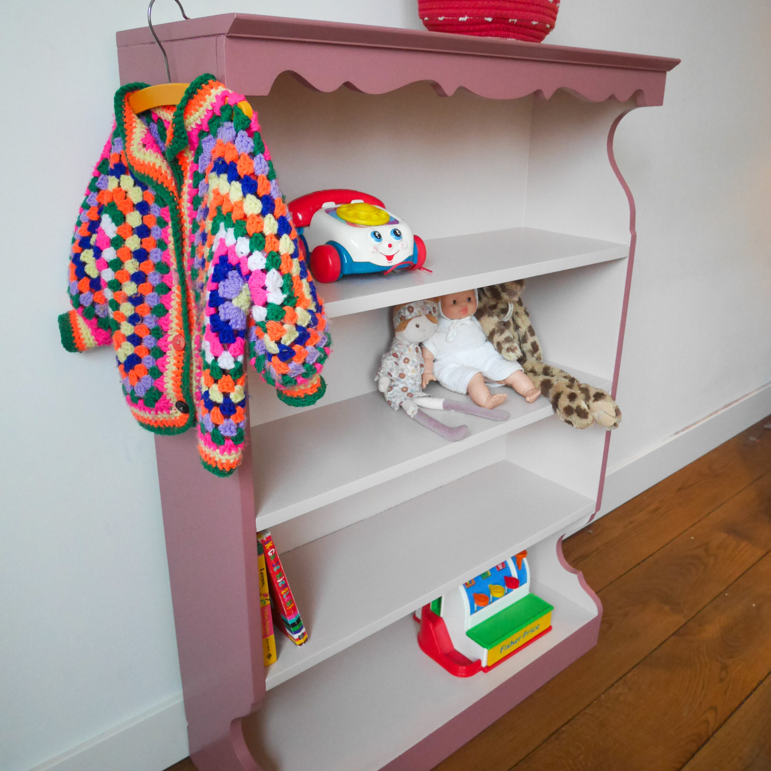 Vintage oudroze boekenkastje voor kinderkamer met sierlijke afwerking en open planken.