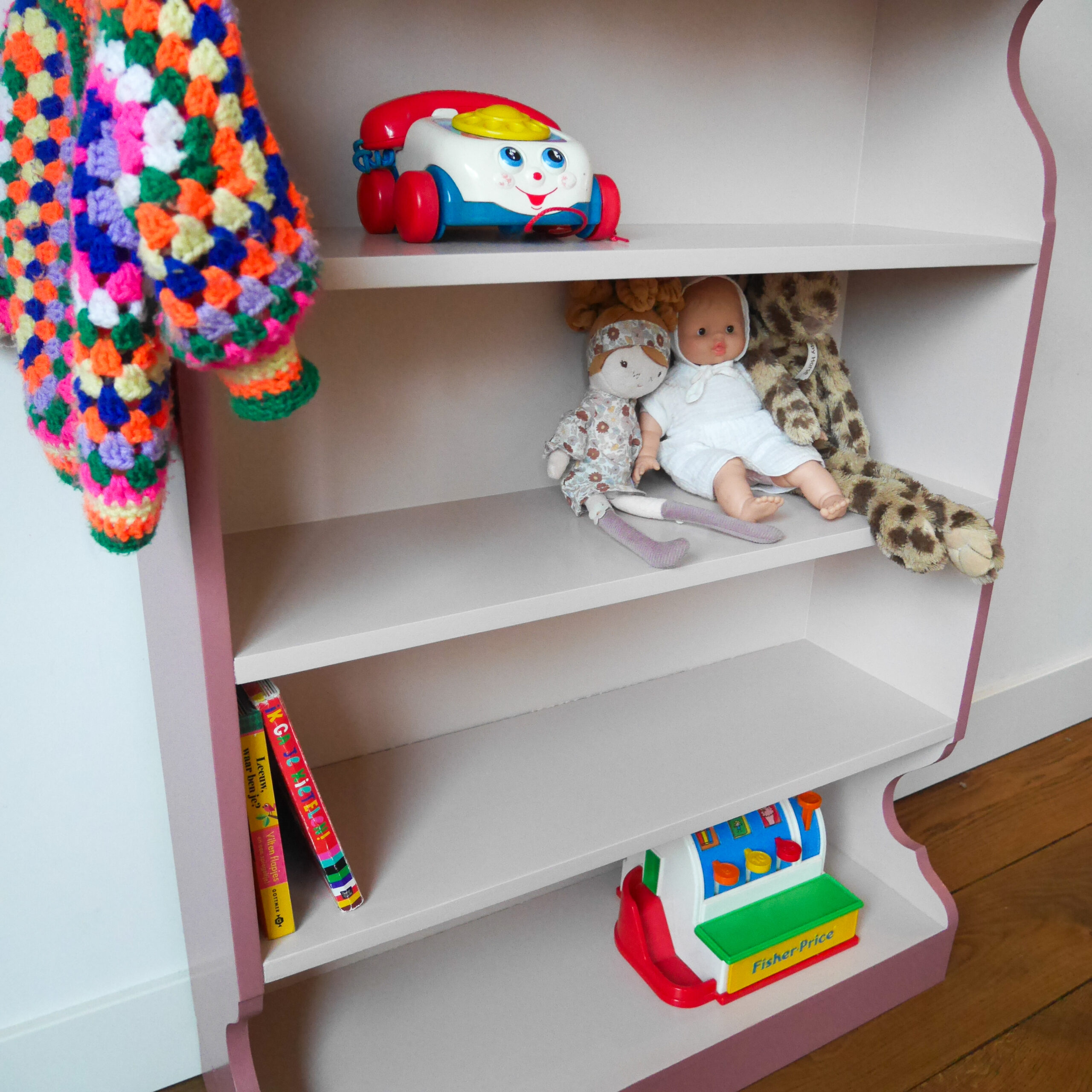 Vintage oudroze boekenkastje voor kinderkamer met sierlijke afwerking en open planken.