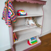 Vintage oudroze boekenkastje voor kinderkamer met sierlijke afwerking en open planken.