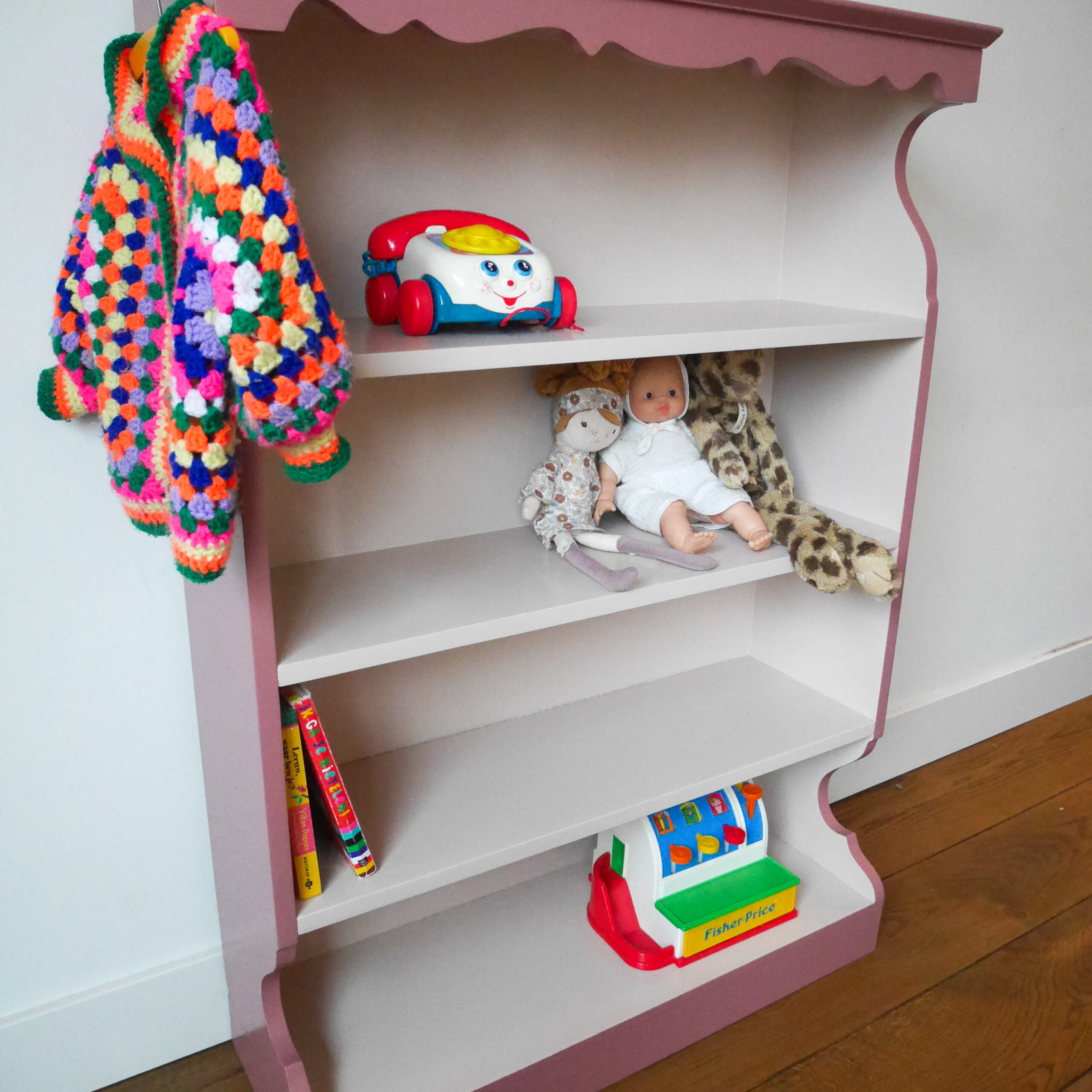Vintage oudroze boekenkastje voor kinderkamer met sierlijke afwerking en open planken.